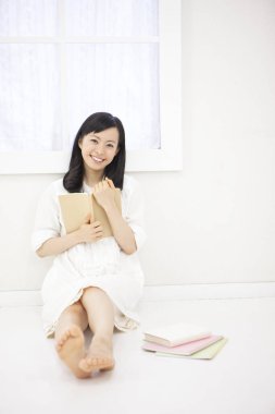 Asyalı kadın evde kitap okuyor.