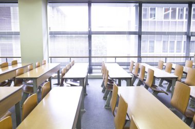 Okuldaki boş sınıfın içinde. Sıralar dolusu tahta masa ve sandalye.