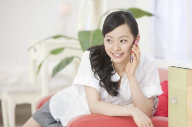 Evdeki kanepede akıllı telefonlu genç bir kadın.