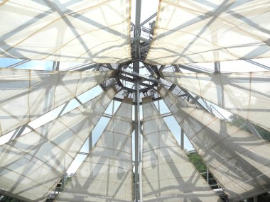 Şeffaf kumaş panelleri destekleyen geometrik metal iskelet boyunca yukarıya doğru bakıyor