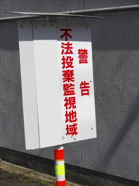 Açık havada cesur kırmızı Japon karakterleri gösteren beyaz uyarı işareti.