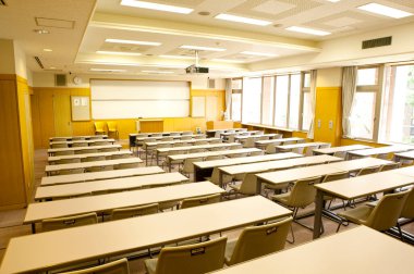 Okuldaki boş sınıfın içinde. Sıralar dolusu tahta masa ve sandalye.