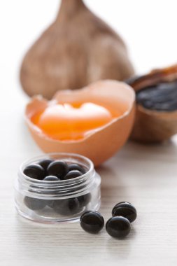 Yumurta sarısı, siyah sarımsak ve ahşap masadaki kapsüllerde besin takviyeleri.
