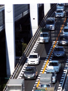 Çok şeritli otoyol, yüksek binalar arasında giden arabaları gösteriyor.