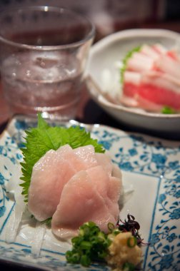 Taze sashimi dilimleri desenli tabakta dinleniyor.