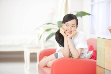 Evdeki kanepede oturan Asyalı kadın. 