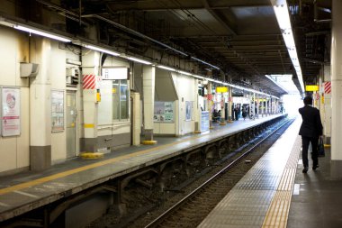 Yükseltilmiş demiryolu kolonları, yoğun Japon şehir manzarası boyunca ritmik bir şekilde yürüyor.
