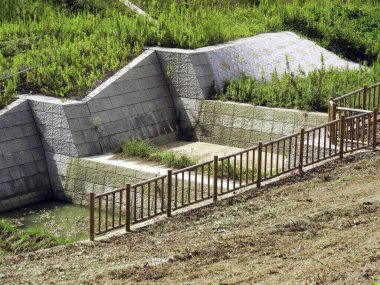 Ahşap çitlerin yanında çimenli yamaçları destekleyen beton istinat duvarı