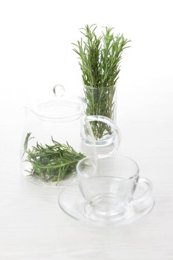 Fresh rosemary sprigs in glass teapot and cup
