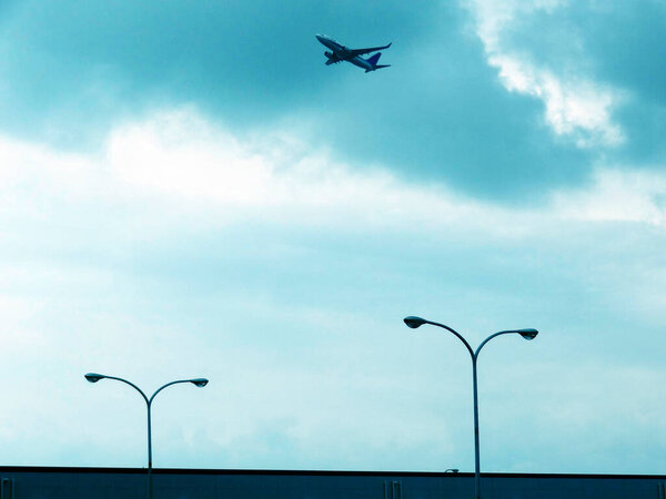 Airplane flying above streetlights under cloudy blue sky