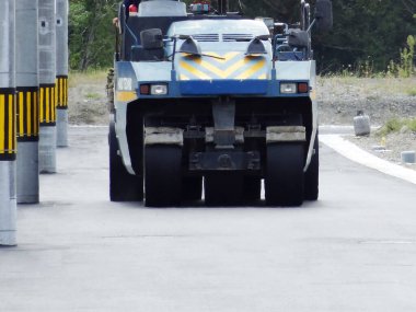 Büyük mavi yol silindiri kaldırımlı sokak boyunca ilerliyor.