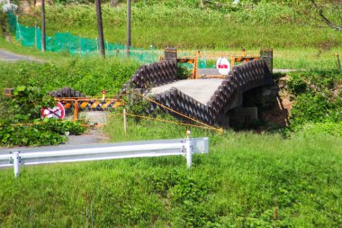 Yeşil çimenler ve uyarı işaretleriyle çevrili terk edilmiş beton köprü.
