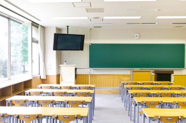 Duvarında yeşil karatahta olan boş sınıfın içi. Sıralar dolusu tahta masa ve sandalye.