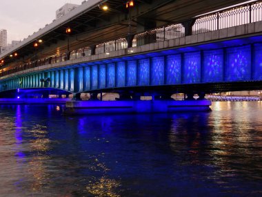 Aydınlatılmış şehir köprüsü durgun su yüzeyine mavi ışık yansıtıyor