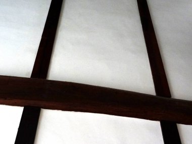 Kapalı alanda beyaz tavan panellerinden geçen ahşap kirişleri gösteriyor.