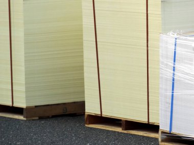 Dışarıdaki ahşap paletlerde duran büyük kağıt yığınları.