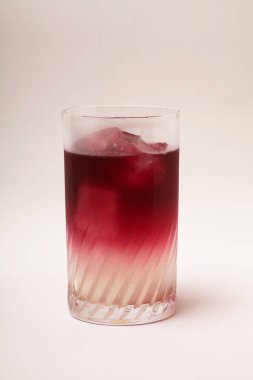 Beyaz zemin üzerinde buz olan bir bardak kırmızı kokteyl.