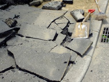 Kırık asfalt parçaları kürek süpürgesiyle kaldırım kenarına saçılmış.