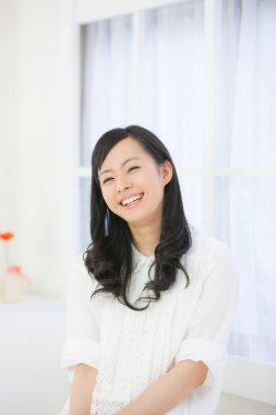 Zarif Asyalı kadın ışıl ışıl beyaz bir odada cazibe ve duruş ile poz verdi..