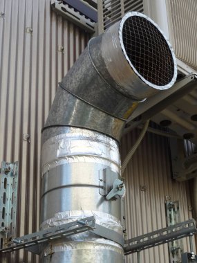 Endüstriyel bina duvarının yanında büyük metalik havalandırma kanalı kıvrılıyor.