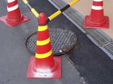 Açık rögar kapağını çevreleyen parlak turuncu trafik konileri