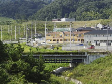 Yeşil tepeler ve elektrik hatlarıyla çevrili küçük köy binaları.