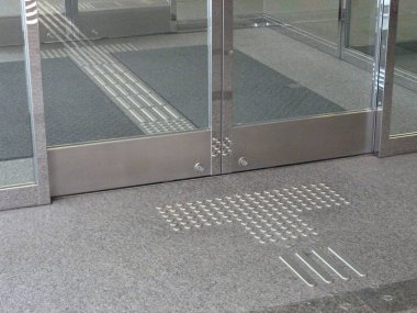 İçerideki cam giriş kapılarına uzanan dokunsal kaldırımlar.