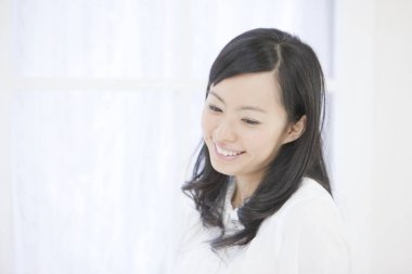 Zarif Asyalı kadın ışıl ışıl beyaz bir odada cazibe ve duruş ile poz verdi..