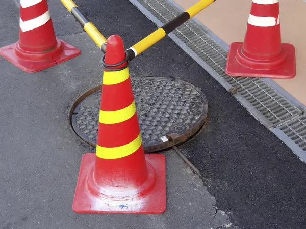 Açık rögar kapağını çevreleyen parlak turuncu trafik konileri