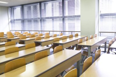 Okuldaki boş sınıfın içinde. Sıralar dolusu tahta masa ve sandalye.