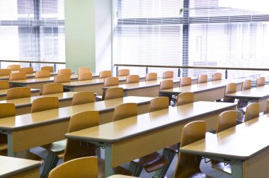 Okuldaki boş sınıfın içinde. Sıralar dolusu tahta masa ve sandalye.