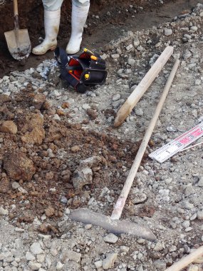 Bot giyen işçiler küreklerin yanında durup kayalık zemin kazıyorlar.