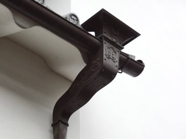 Beyaz bina duvarına bağlanmış süslü metal olukları gösteren yakın plan