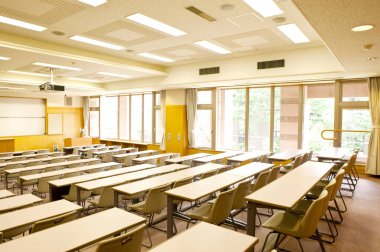 Okuldaki boş sınıfın içinde. Sıralar dolusu tahta masa ve sandalye.