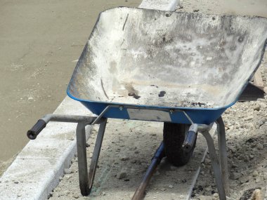 Bitmemiş beton kaldırımın kenarında duran eski mavi el arabası.