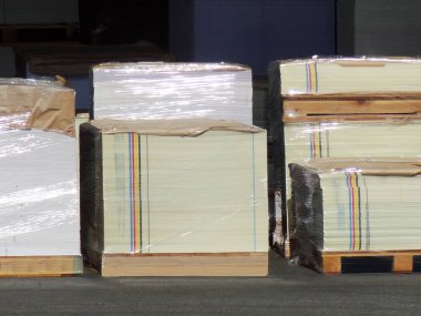 Plastiğe sarılı büyük kağıt yığınları dışarıda duruyor.