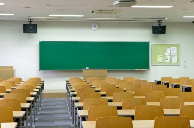 Duvarında yeşil karatahta olan boş sınıfın içi. Sıralar dolusu tahta masa ve sandalye.