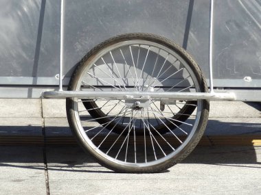 Tek bisiklet tekerleği dışarıda metal korkuluklara dayanıyor.