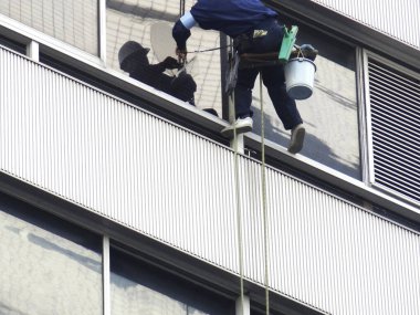 Pencere temizleyicisi uzun binanın dışında asılı cam yüzeyi yıkıyor.