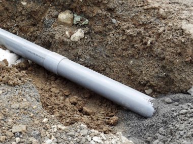Çamurla çevrili gri boru çukurda yatıyor.