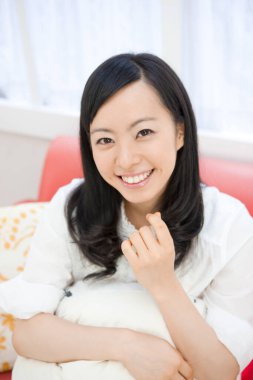 Göz kamaştırıcı Asyalı bir kadının portresi. Geniş, parlak, beyaz bir ortamda rahatça poz veriyor..