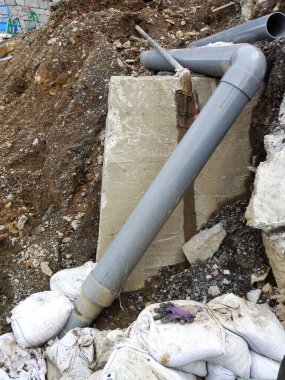 İnşaat alanında kayalarla birleşen büyük gri drenaj boruları.