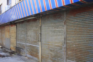 Gündüz vakti çizgili tentenin altındaki kapalı metal dükkan panjurları.