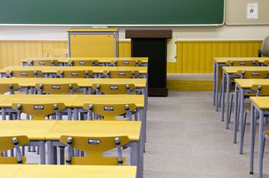 Duvarında yeşil karatahta olan boş sınıfın içi. Sıralar dolusu tahta masa ve sandalye.