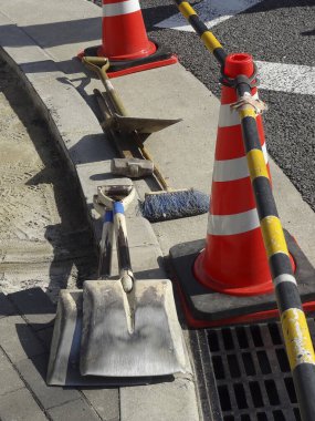 Kürekler ve trafik konileri beton kaldırım kenarında dinleniyor.