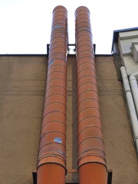 Dış bina duvarına bağlı uzun turuncu sanayi havalandırma boruları.