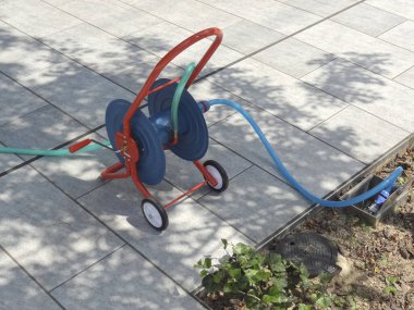 Asfalt kaldırımın yanında duran bahçe hortumu makarası.