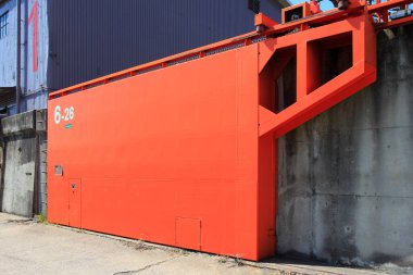 Büyük endüstriyel turuncu yapı beton duvara dayanıyor.