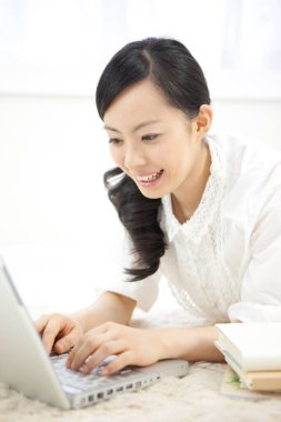 Göz kamaştırıcı bir Japon kadının portresi. Parlak beyaz bir odada dizüstü bilgisayarla çalışıyor..