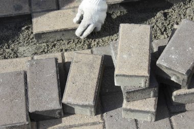 Dışarıda eldivenli ellerle beton tuğlalar döşüyorlar.